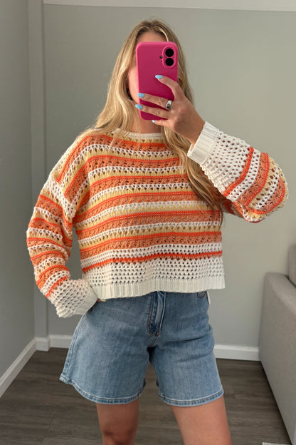 person wearing a crochet knit orange sweater in a mirror photo