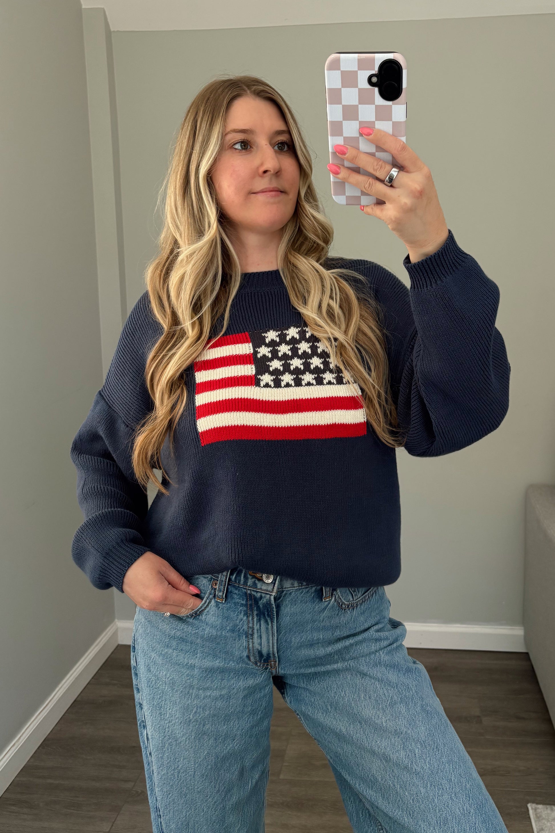 Person wearing a navy sweater with an American flag design, standing in a room.