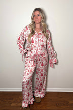 Woman wearing a red and white patterned pajama set against a plain wall.