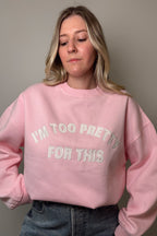 Close-up of the pink Too Pretty sweatshirt showing the embroidered I'm Too Pretty For This lettering and ribbed crew neckline.

