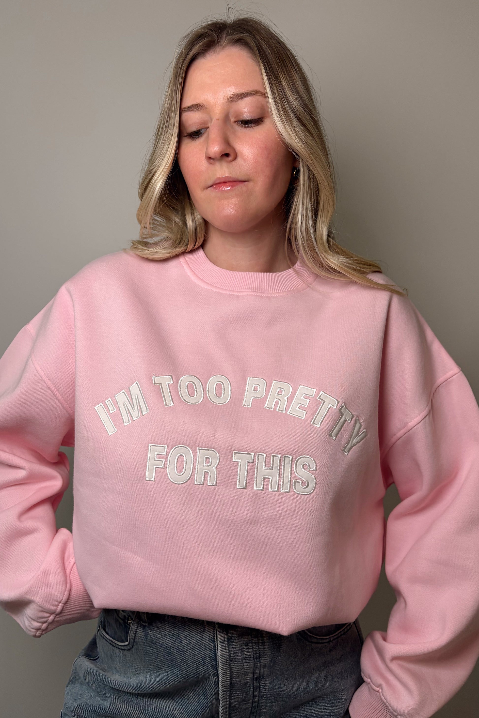 Person wearing a pink sweatshirt with "I'm too pretty for this" text, standing against a plain background