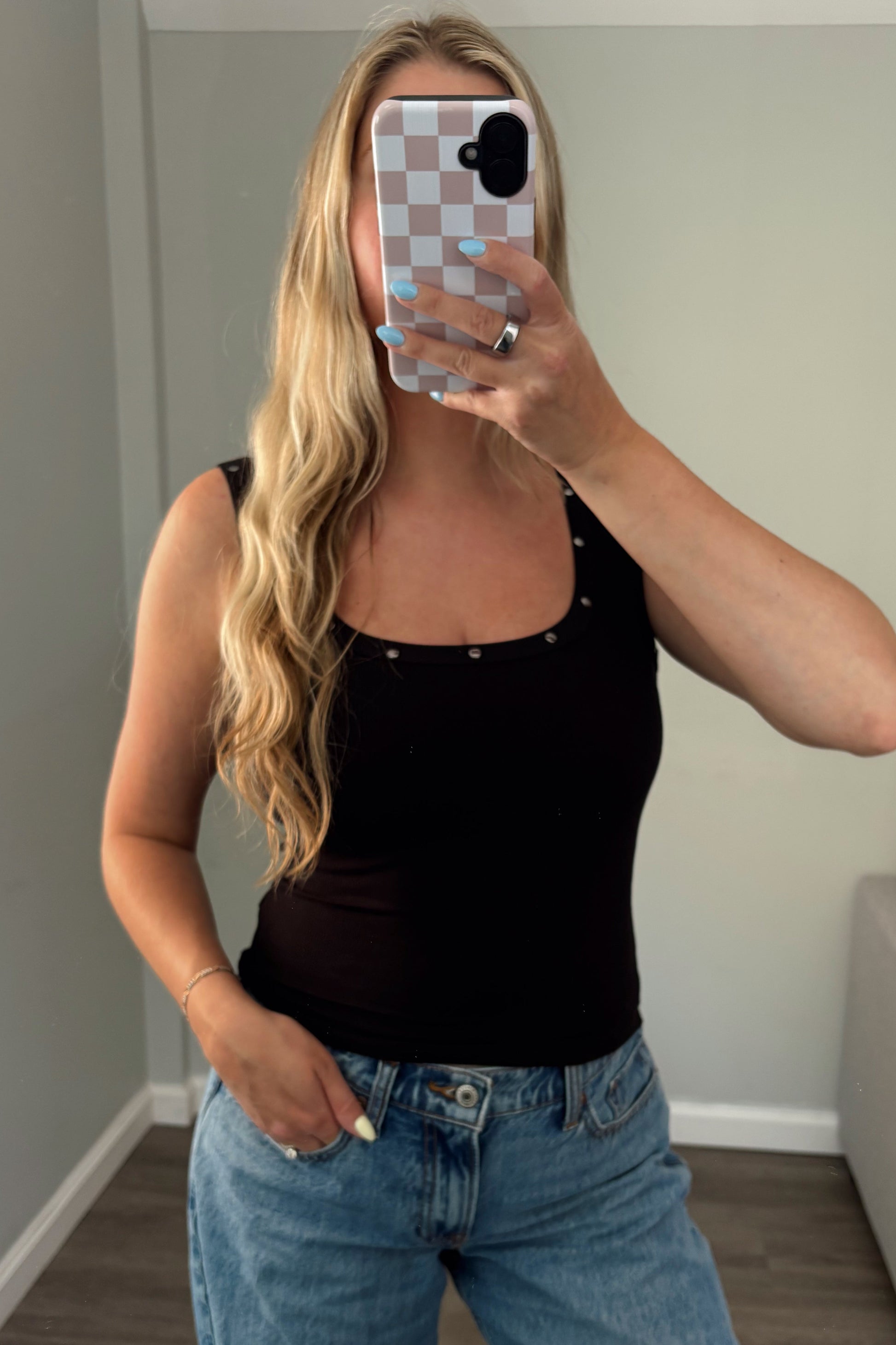 Person taking a mirror selfie wearing a black top and blue jeans in a room.