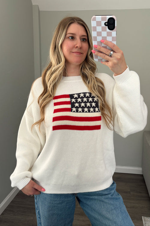 Front view of white American flag sweater showing its relaxed fit, crew neckline, and ribbed hem