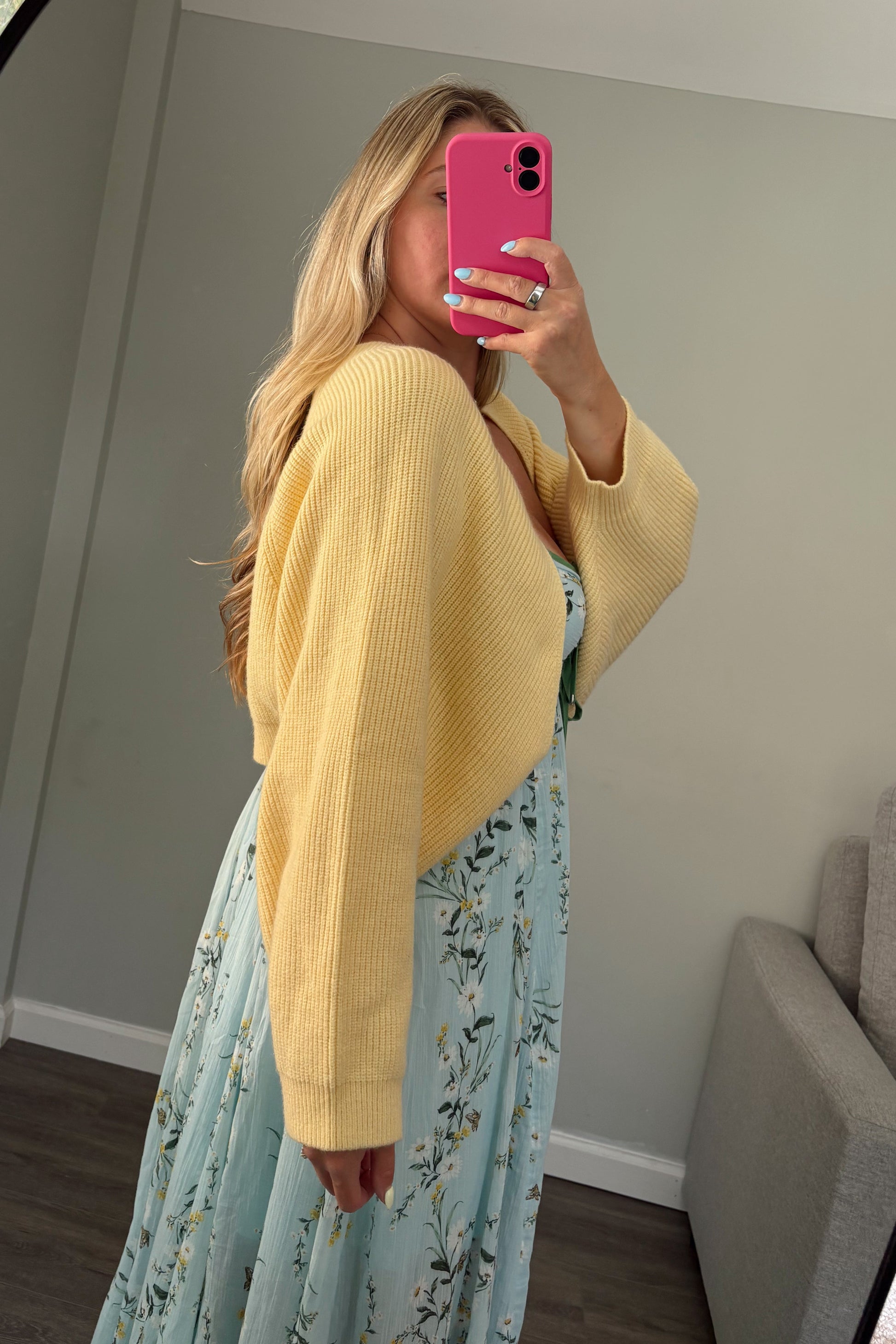 Person wearing a yellow cardigan and floral dress taking a mirror selfie.
