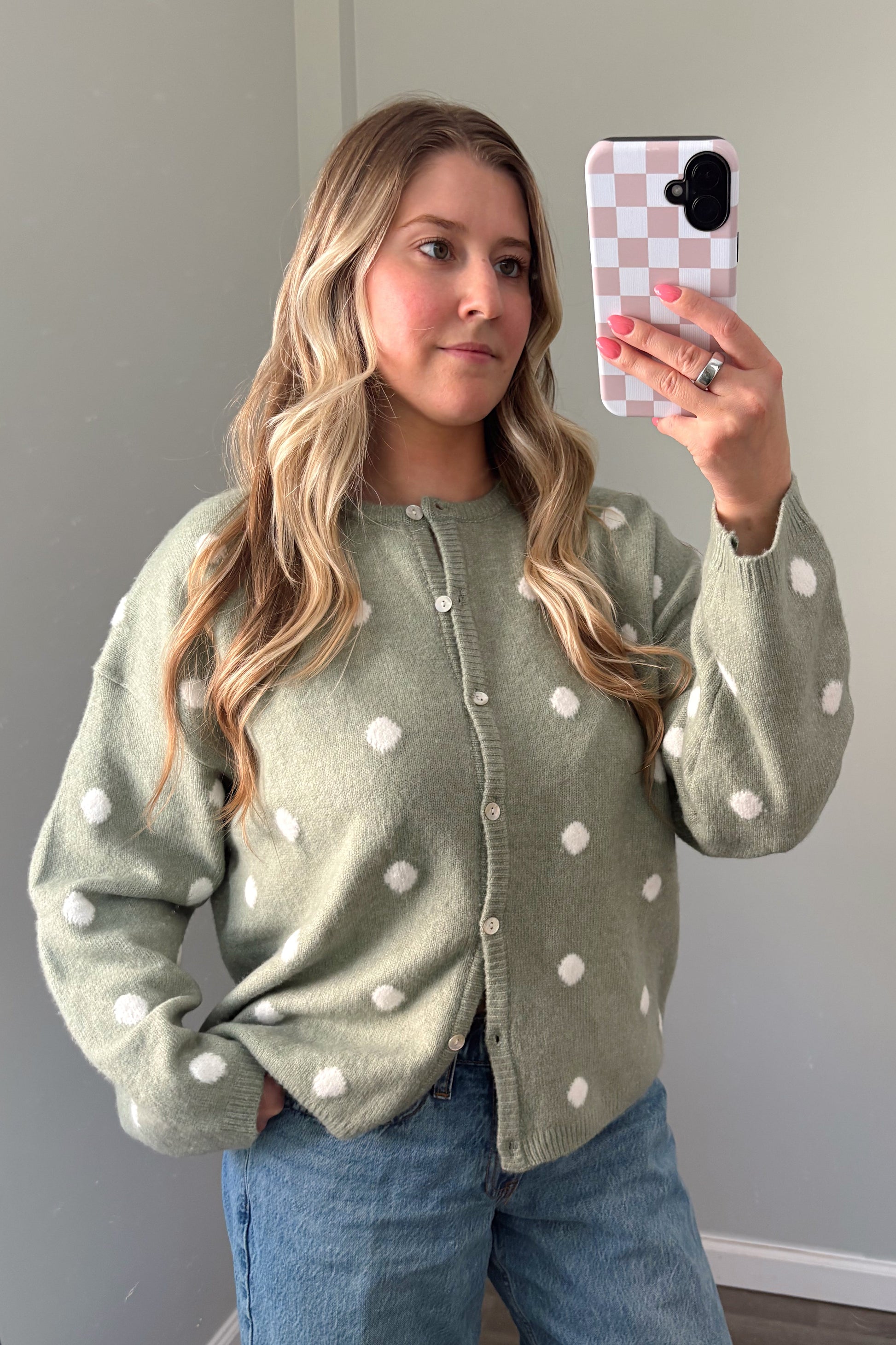 person wearing a sage green polka dot cardigan in a mirror photo