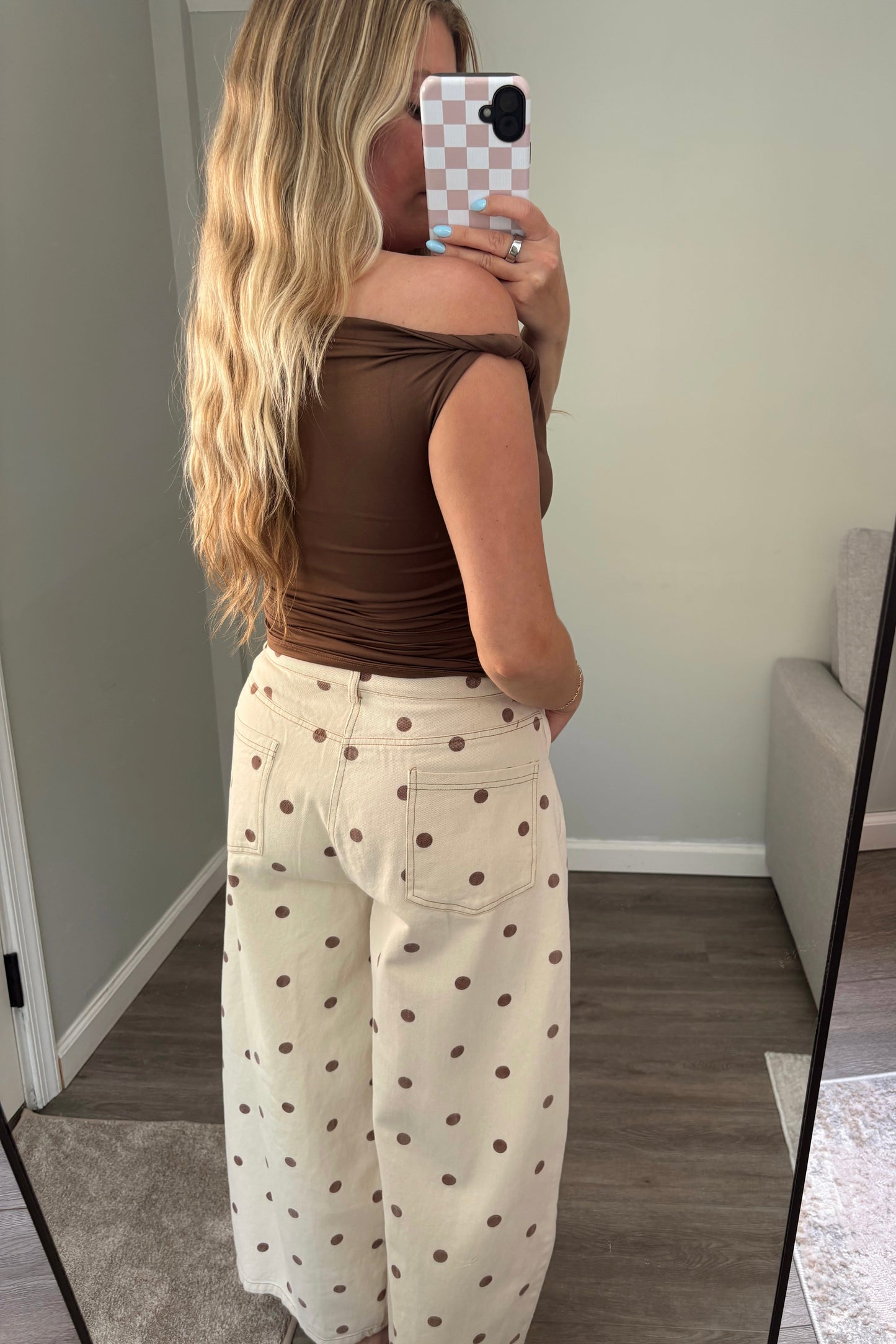 Woman taking a mirror selfie wearing a brown top and white pants with black polka dots.