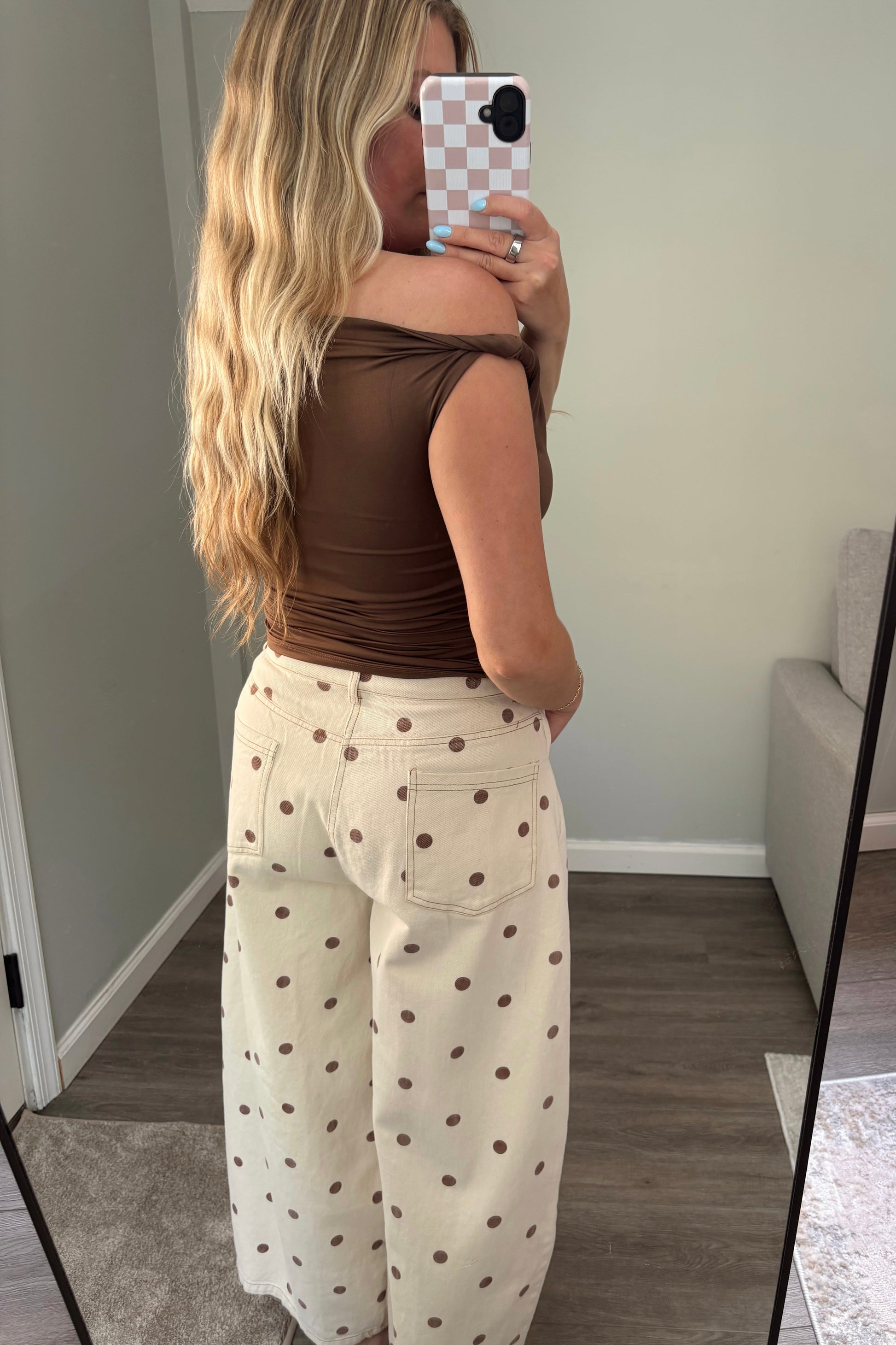 Woman taking a mirror selfie wearing a brown top and white pants with black polka dots.