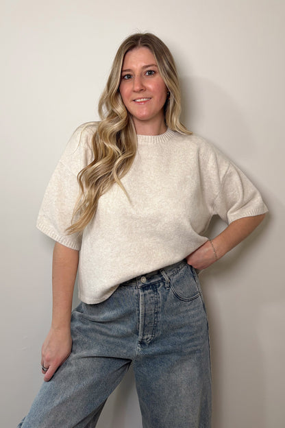 Woman wearing a white sweater and blue jeans against a plain background