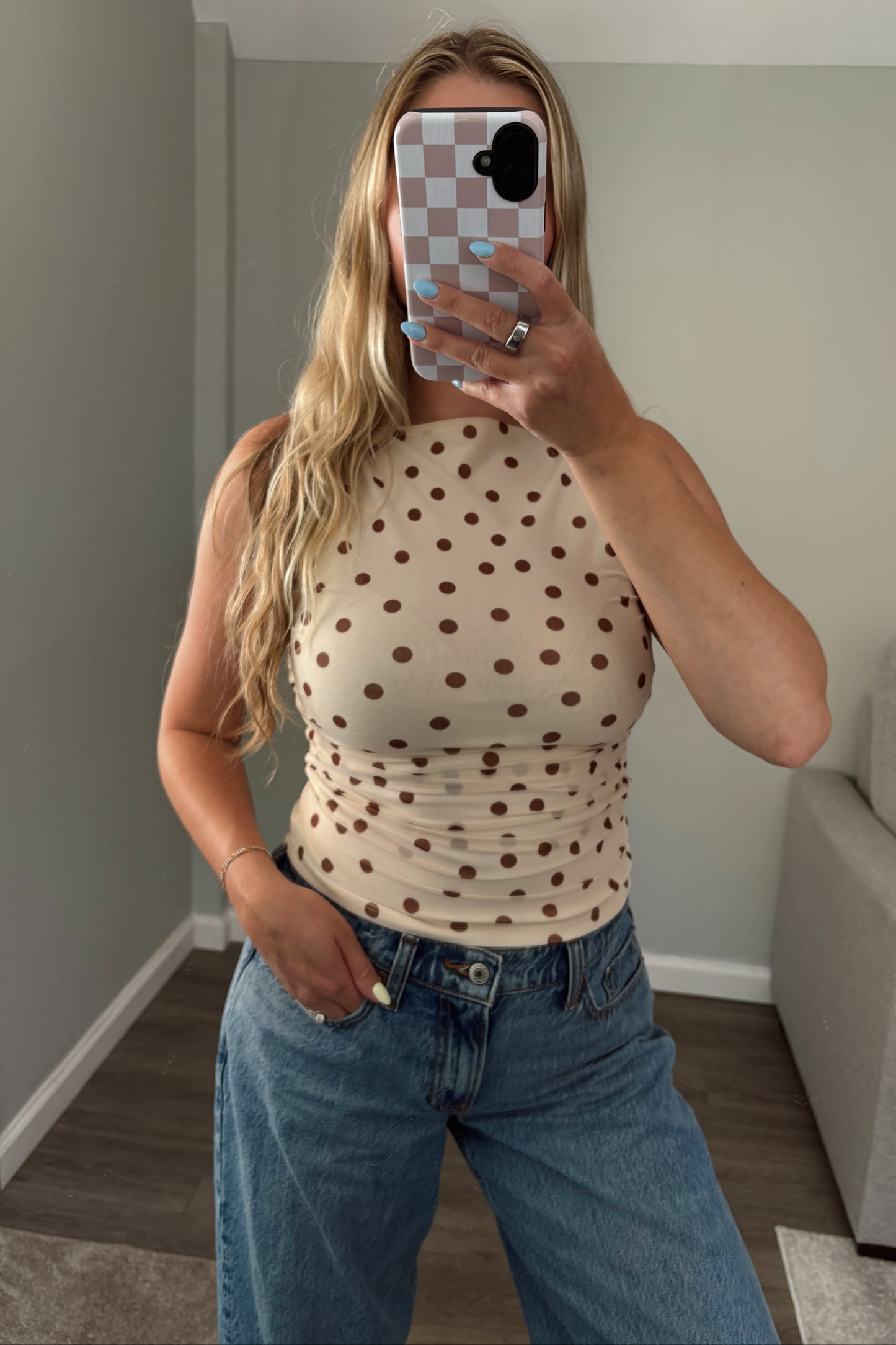 Person wearing a polka dot top and jeans taking a mirror selfie.