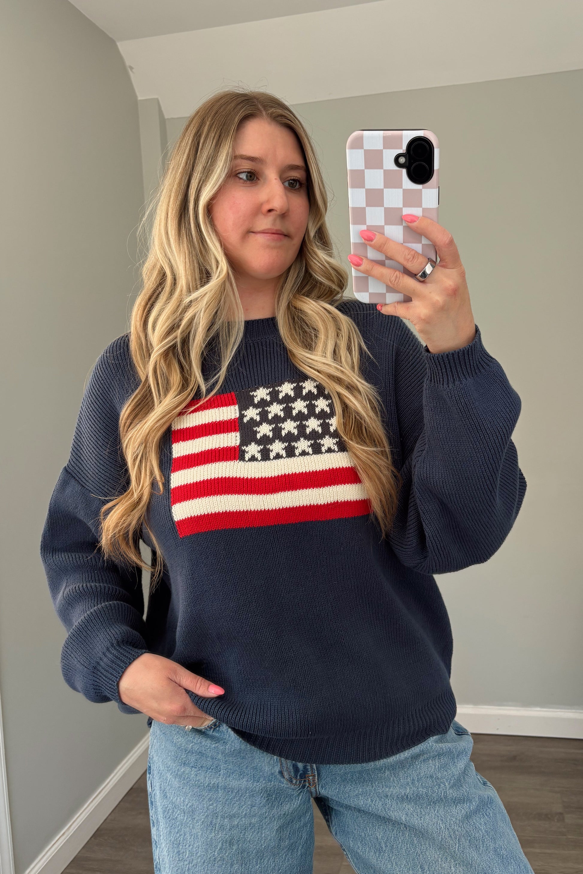 Person wearing a navy sweater with an American flag design, taking a mirror selfie.