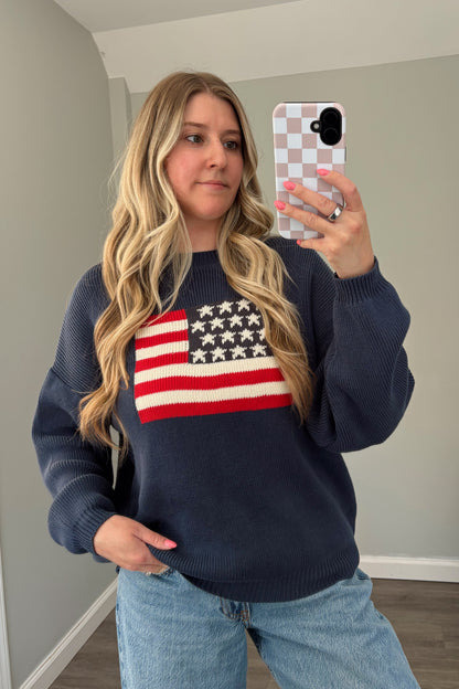 Person wearing a navy sweater with an American flag design, taking a mirror selfie.