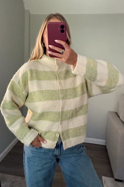 A woman takes a mirror selfie wearing a fuzzy, long-sleeve button-up cardigan with horizontal light green and cream stripes, paired with blue jeans.