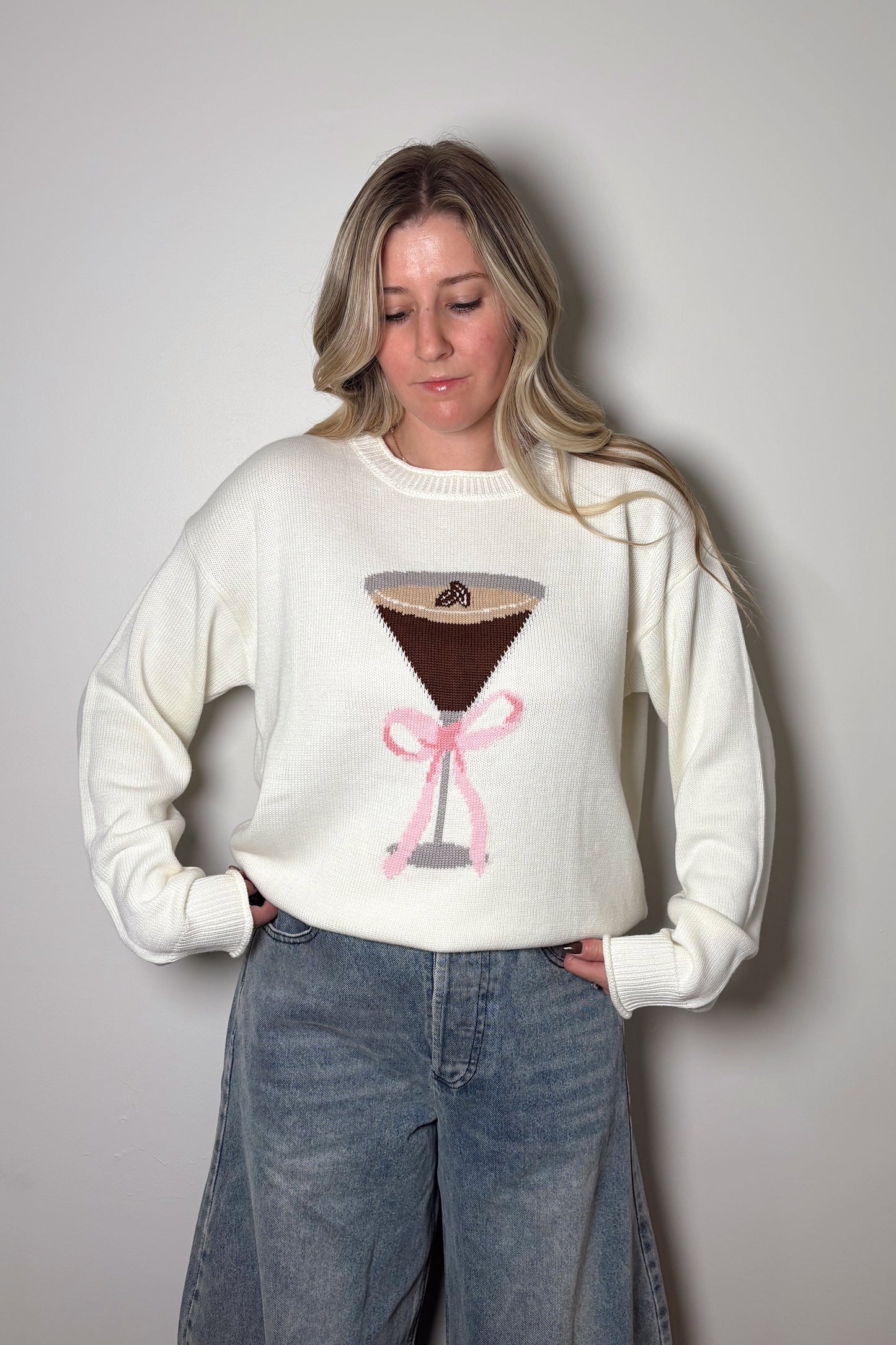 Person wearing a white sweater with a graphic design on a plain background