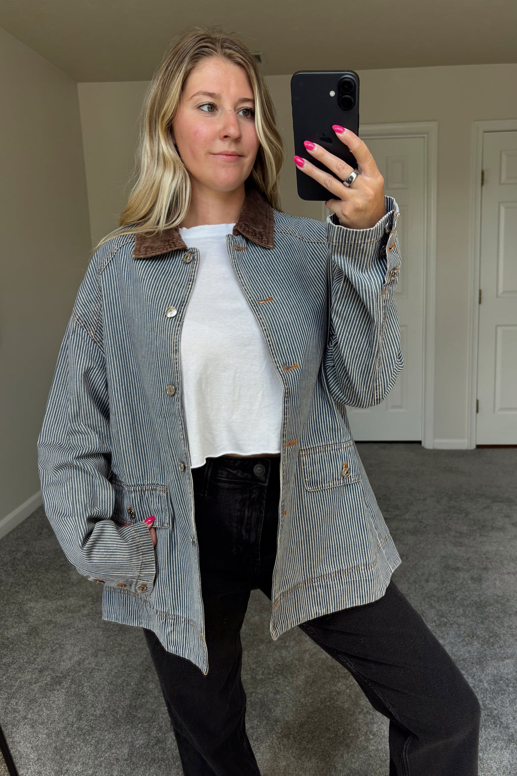 Derby striped denim barn jacket worn open over a white tee and black jeans, with one hand in a front pocket and the brown corduroy collar visible.

