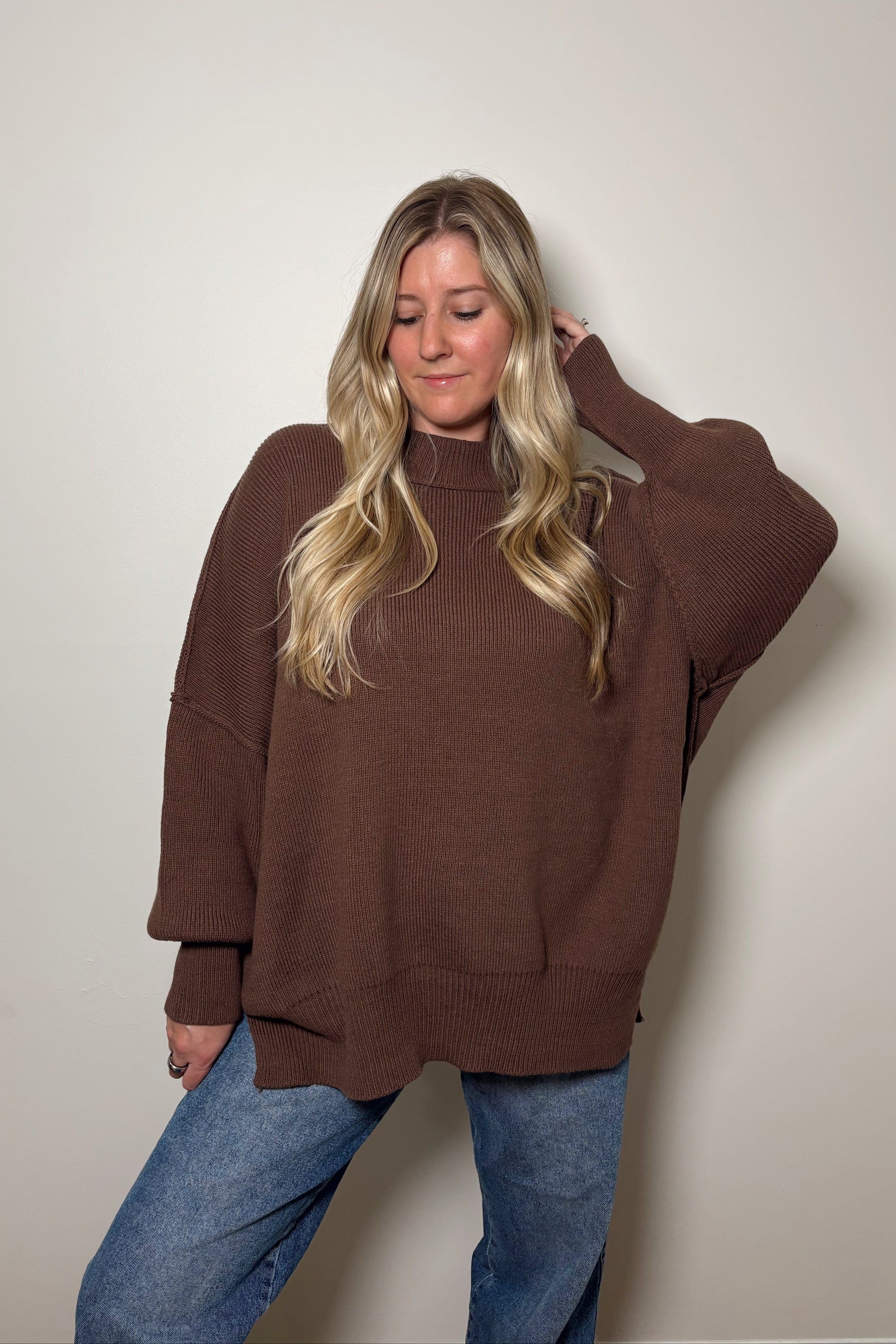 Person wearing a brown oversized sweater and blue jeans against a plain background