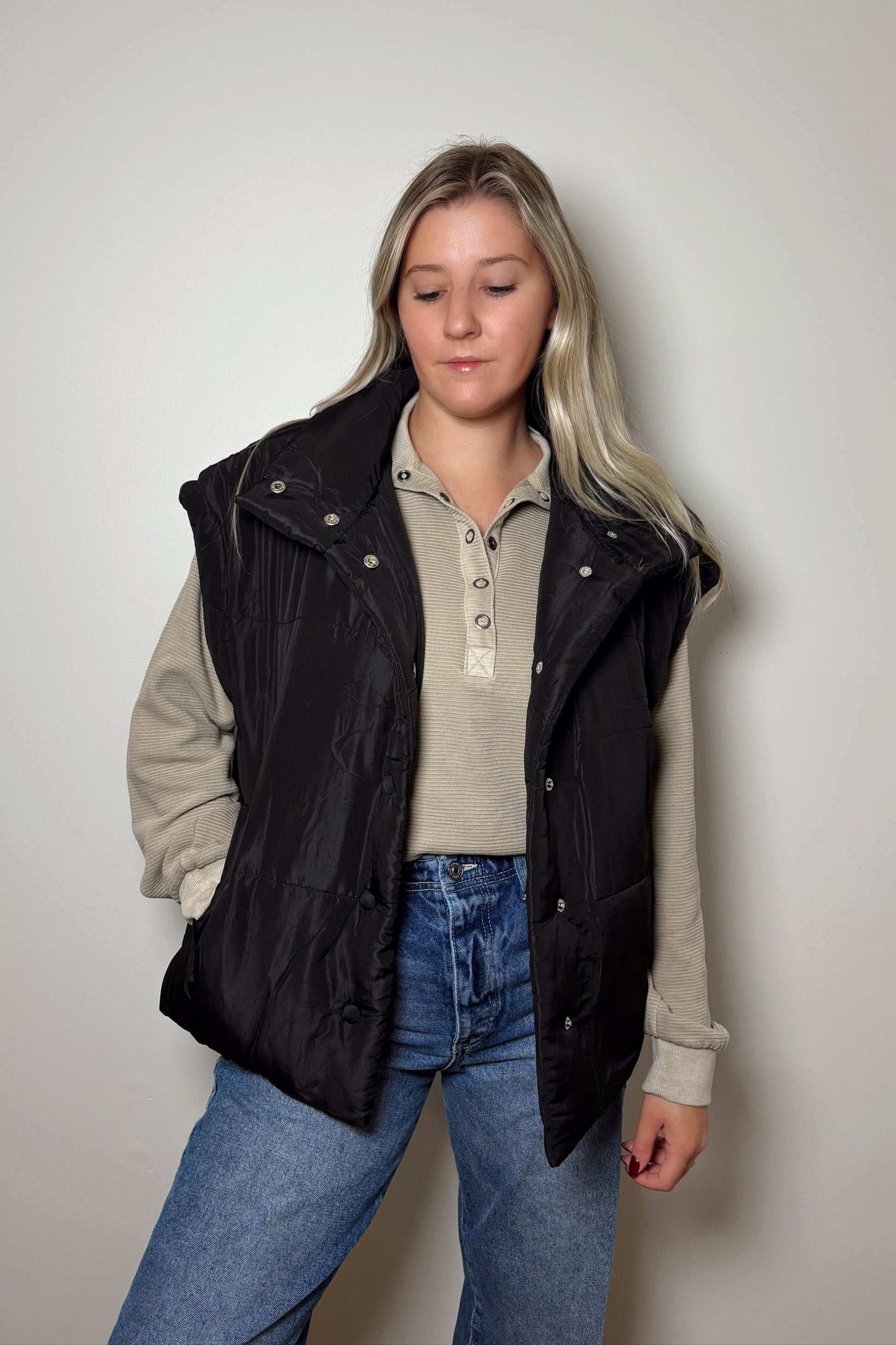 Person wearing a black vest over a beige jacket with a plain background