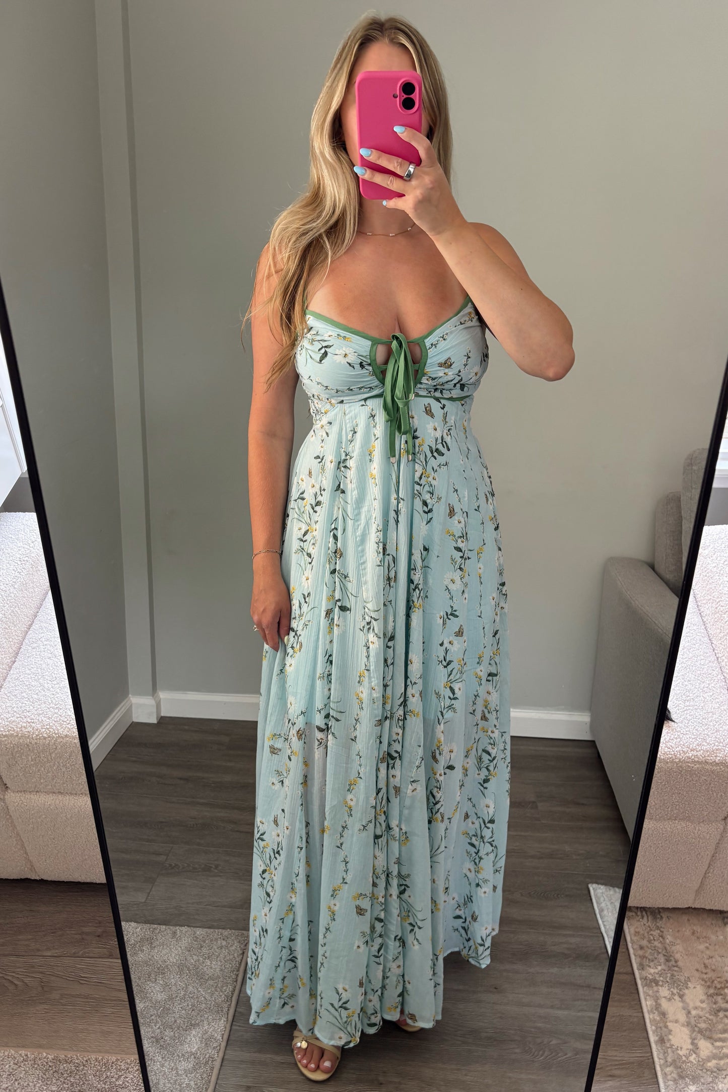 Woman wearing a light blue floral dress standing in front of a mirror.