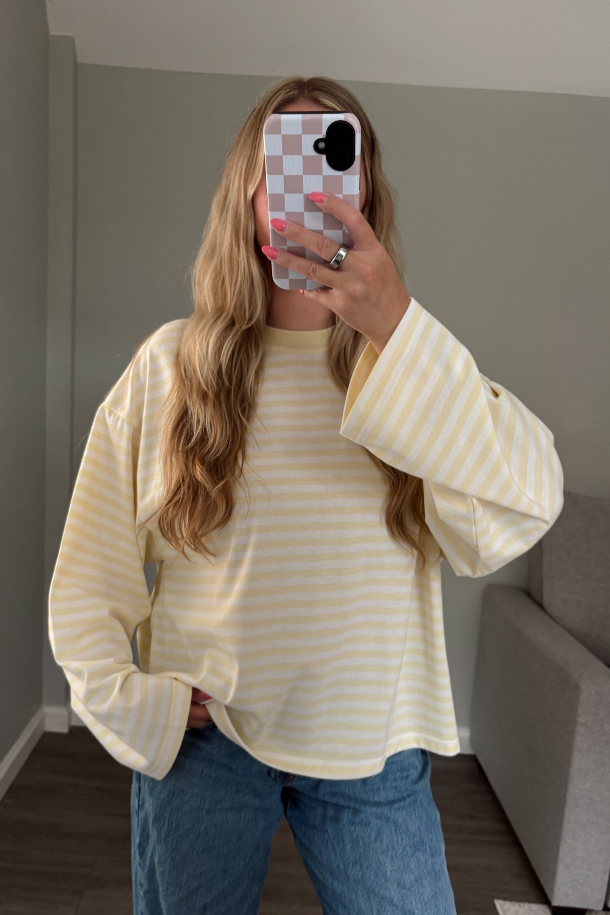 Person wearing a yellow and white striped shirt and blue jeans taking a mirror selfie.