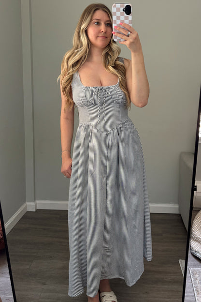 Woman taking a mirror selfie wearing a blue stripe dress in a room with a window and rug.