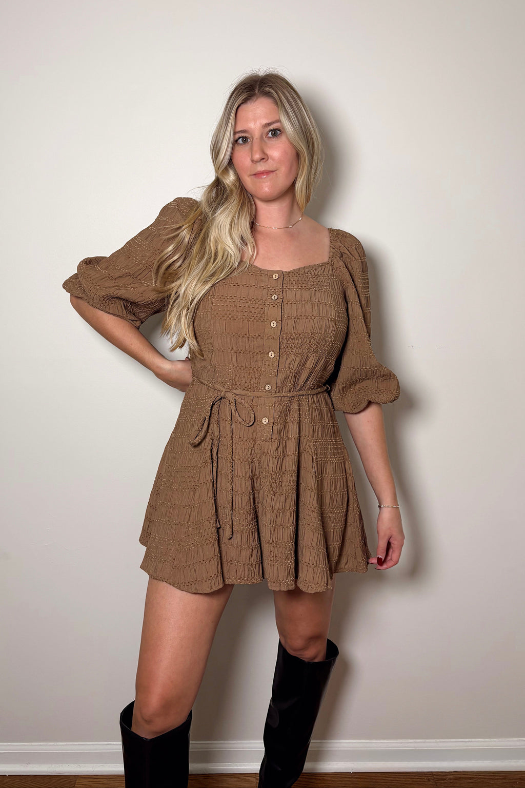 Brielle brown textured romper with puff sleeves, front buttons, and a braided tie belt, styled with tall black boots.

