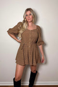 Brielle brown textured romper with puff sleeves, front buttons, and a braided tie belt, styled with tall black boots.

