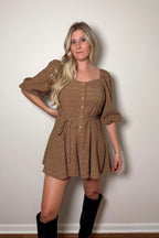 Brielle brown textured romper with puff sleeves, front buttons, and a braided tie belt, styled with tall black boots.

