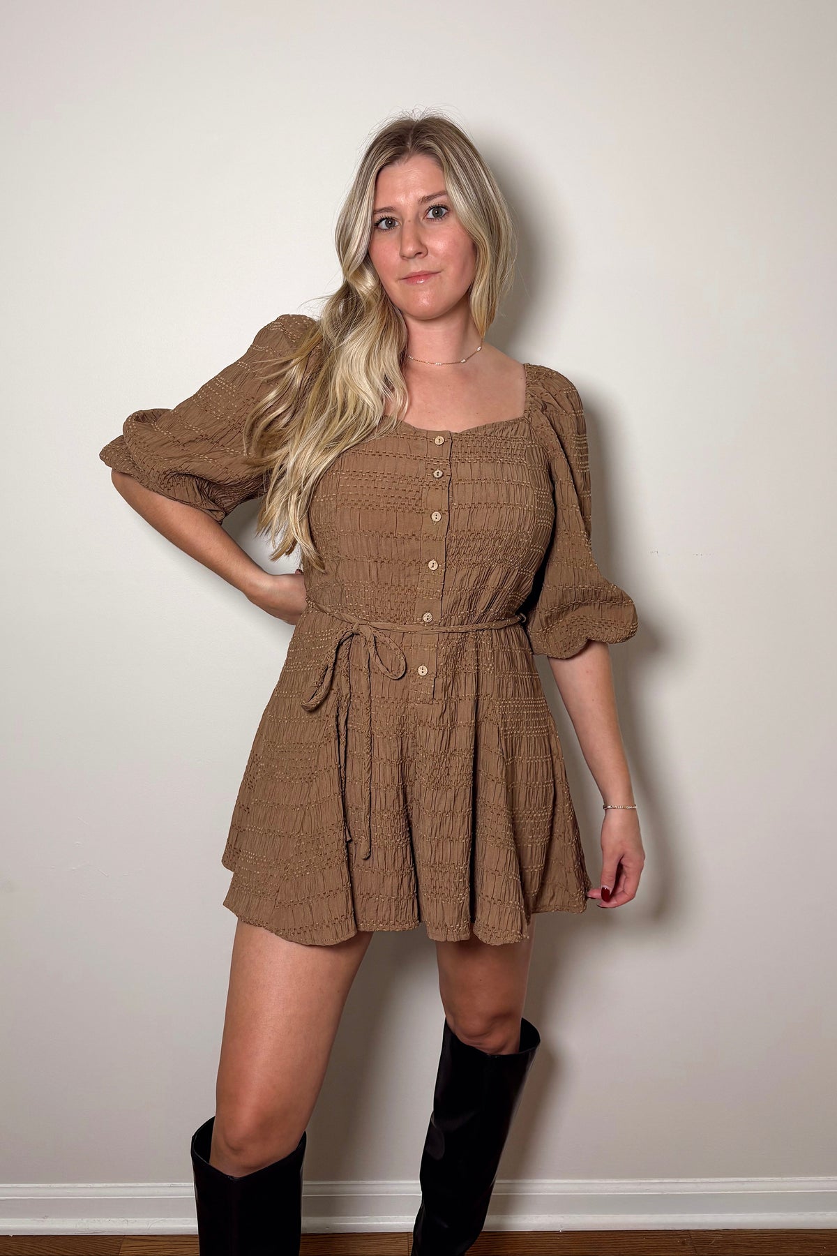 Brielle brown textured romper with puff sleeves, front buttons, and a braided tie belt, styled with tall black boots.

