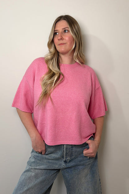 Person wearing a pink oversized shirt and blue jeans against a plain background