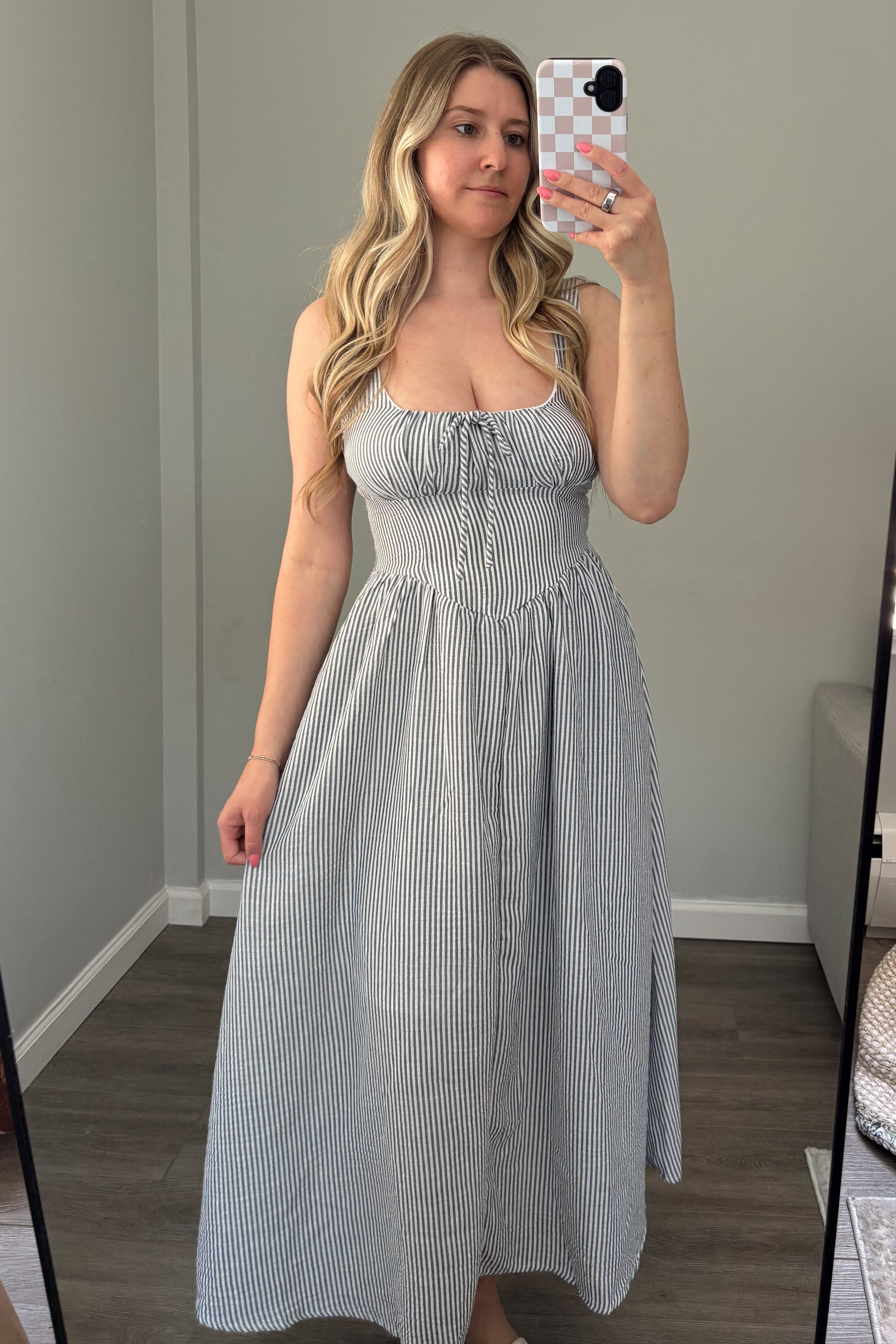 Woman taking a mirror selfie wearing a light blue dress in a room with a window.