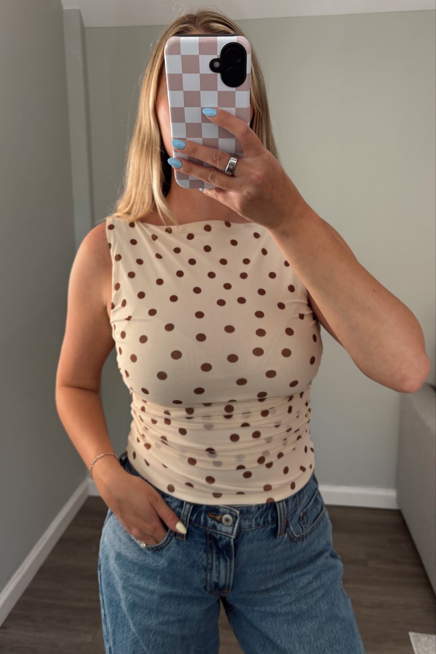 Person wearing a polka dot tank top and jeans taking a mirror selfie.