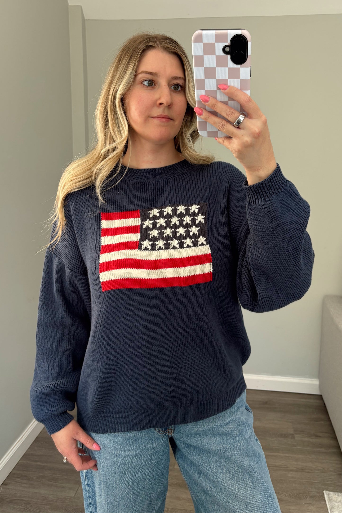 Person wearing a navy sweater with an American flag design, taking a mirror selfie.