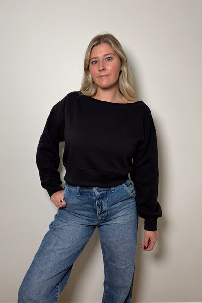 Person wearing a black sweater and blue jeans against a plain background
