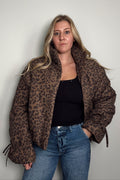 Model wearing the Coco Leopard Puffer Jacket open over a black top, a leopard print puffer with a stand collar and side pockets, styled with blue jeans