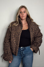 Model wearing the Coco Leopard Puffer Jacket open over a black top, a leopard print puffer with a stand collar and side pockets, styled with blue jeans