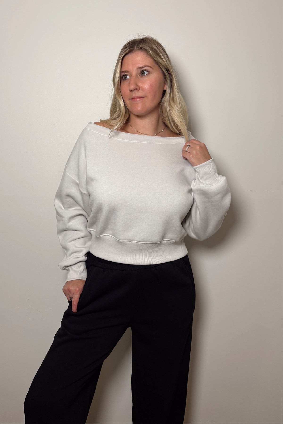 Haven stone cropped pullover with the model holding the wide boat neckline, paired with black pants.

