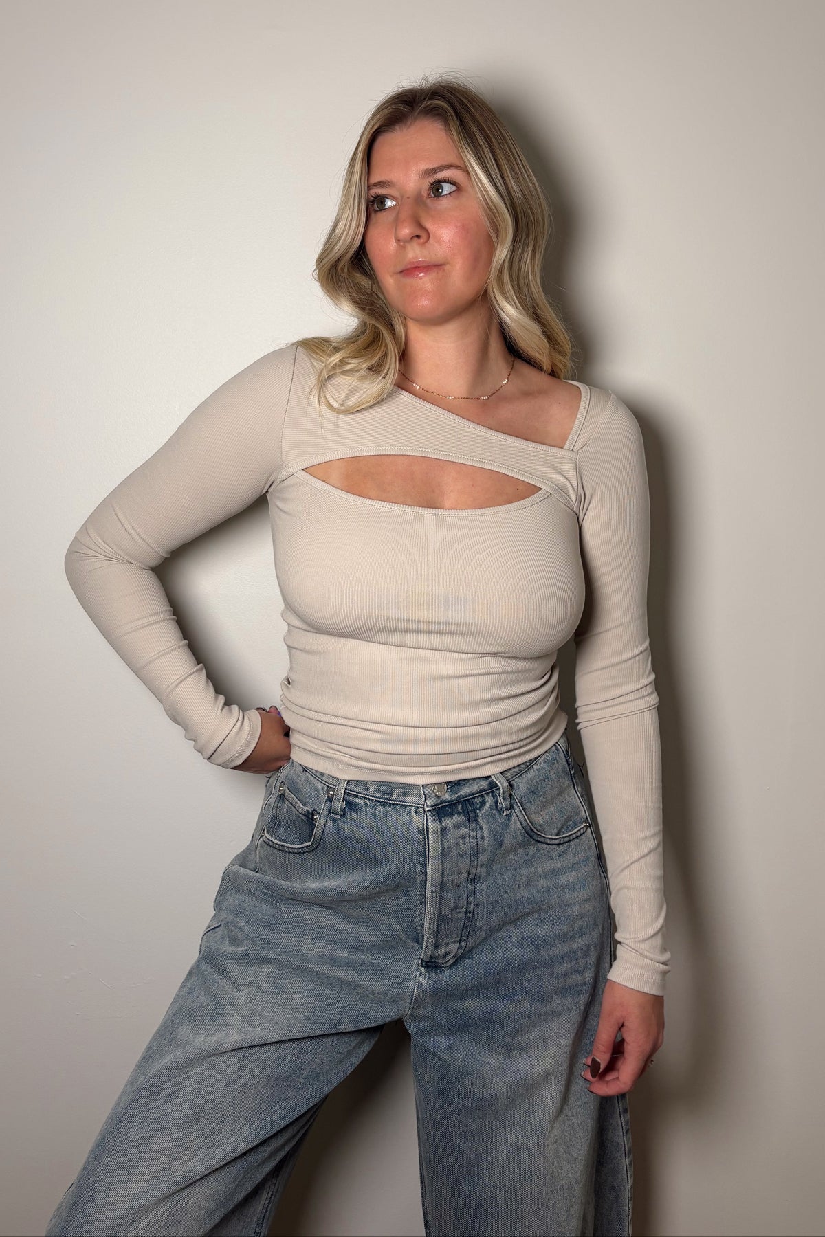 Onyx bone ribbed long-sleeve top with an asymmetrical neckline and chest cutout, styled with light-wash jeans.

