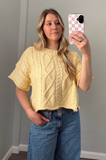 Person wearing a yellow cable knit sweater and blue jeans taking a mirror selfie.
