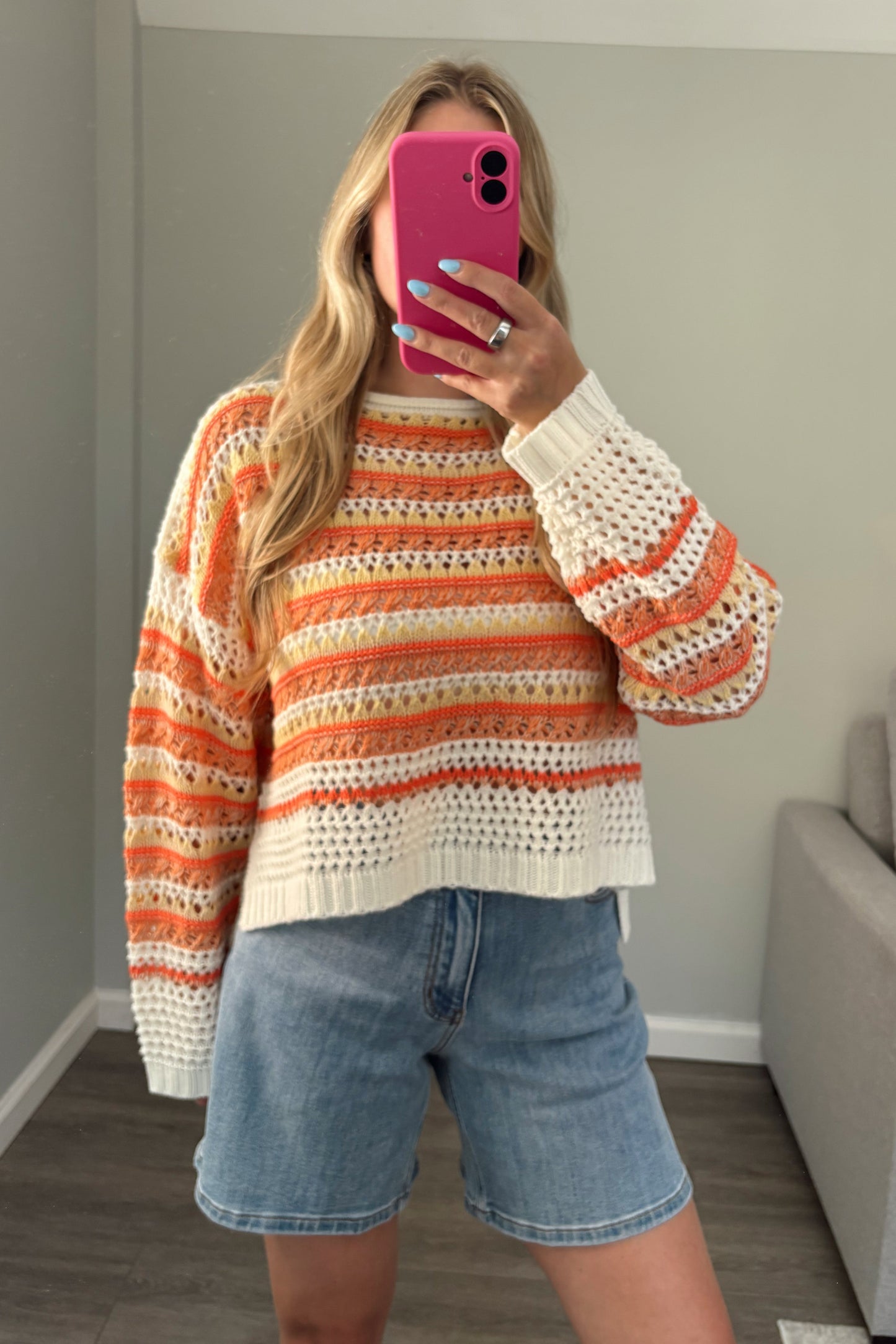 person wearing a crochet orange sweater in a mirror photo