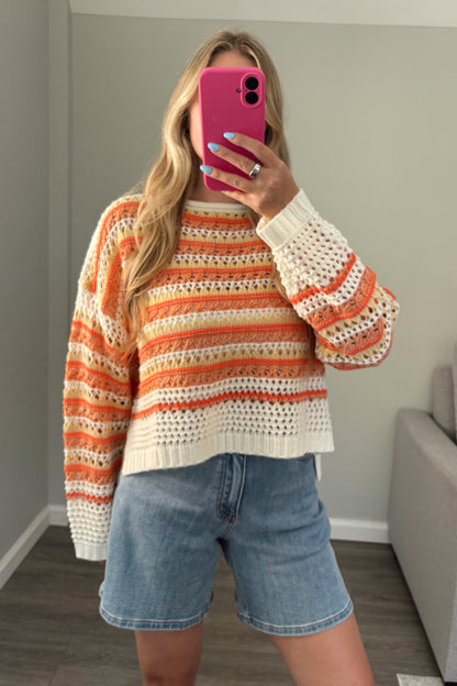 person wearing a crochet orange sweater in a mirror photo