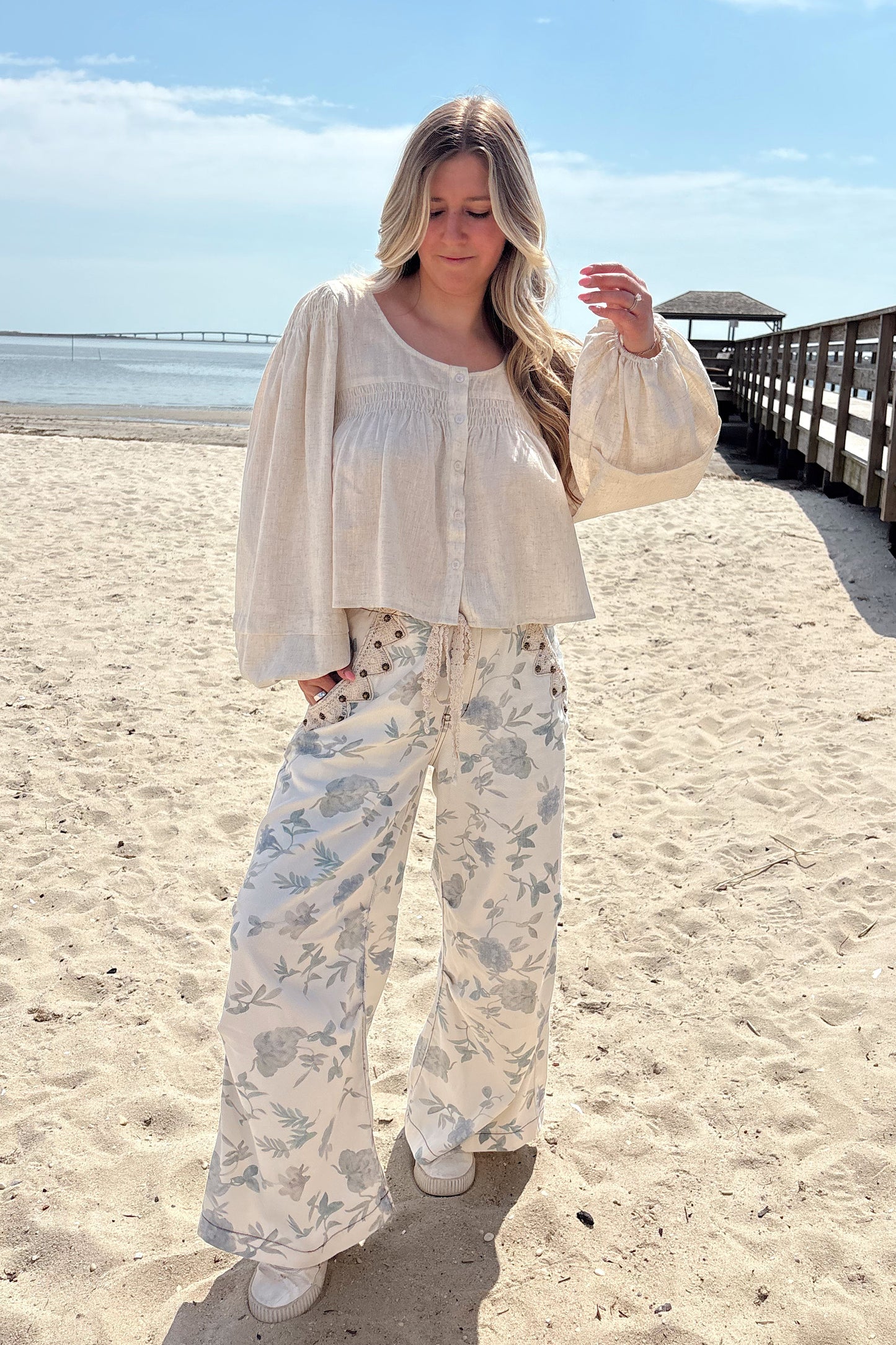 Person wearing a white shirt with floral patterned pants on a beach.