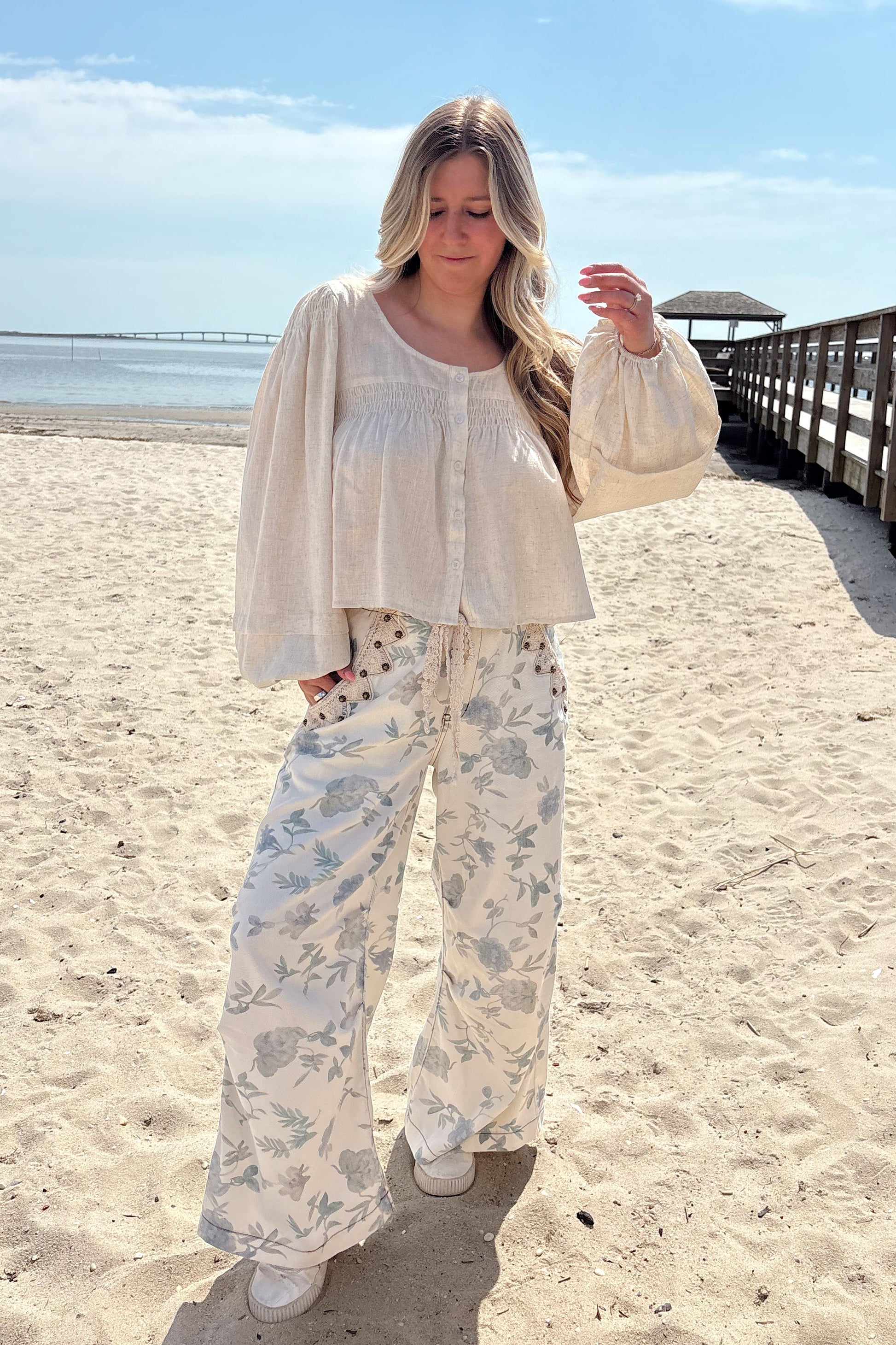 Person wearing a white shirt with floral patterned pants on a beach.