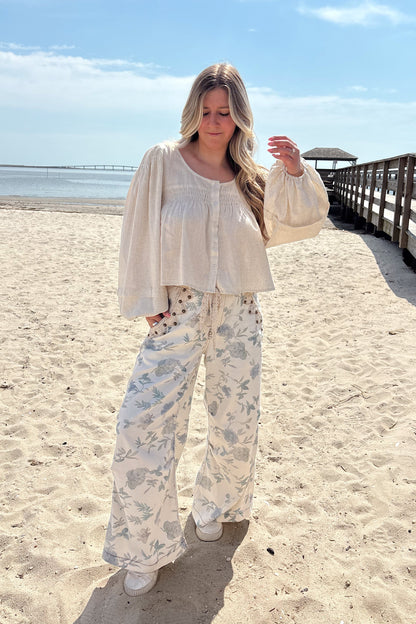 Person wearing a white outfit with floral pants on a sandy beach.