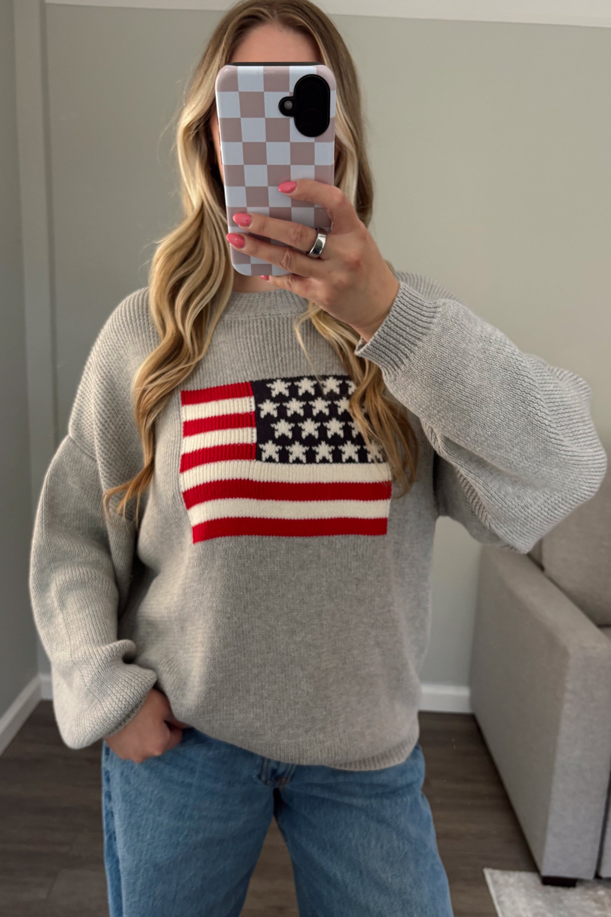 Person wearing a gray sweater with an American flag design, taking a mirror selfie.