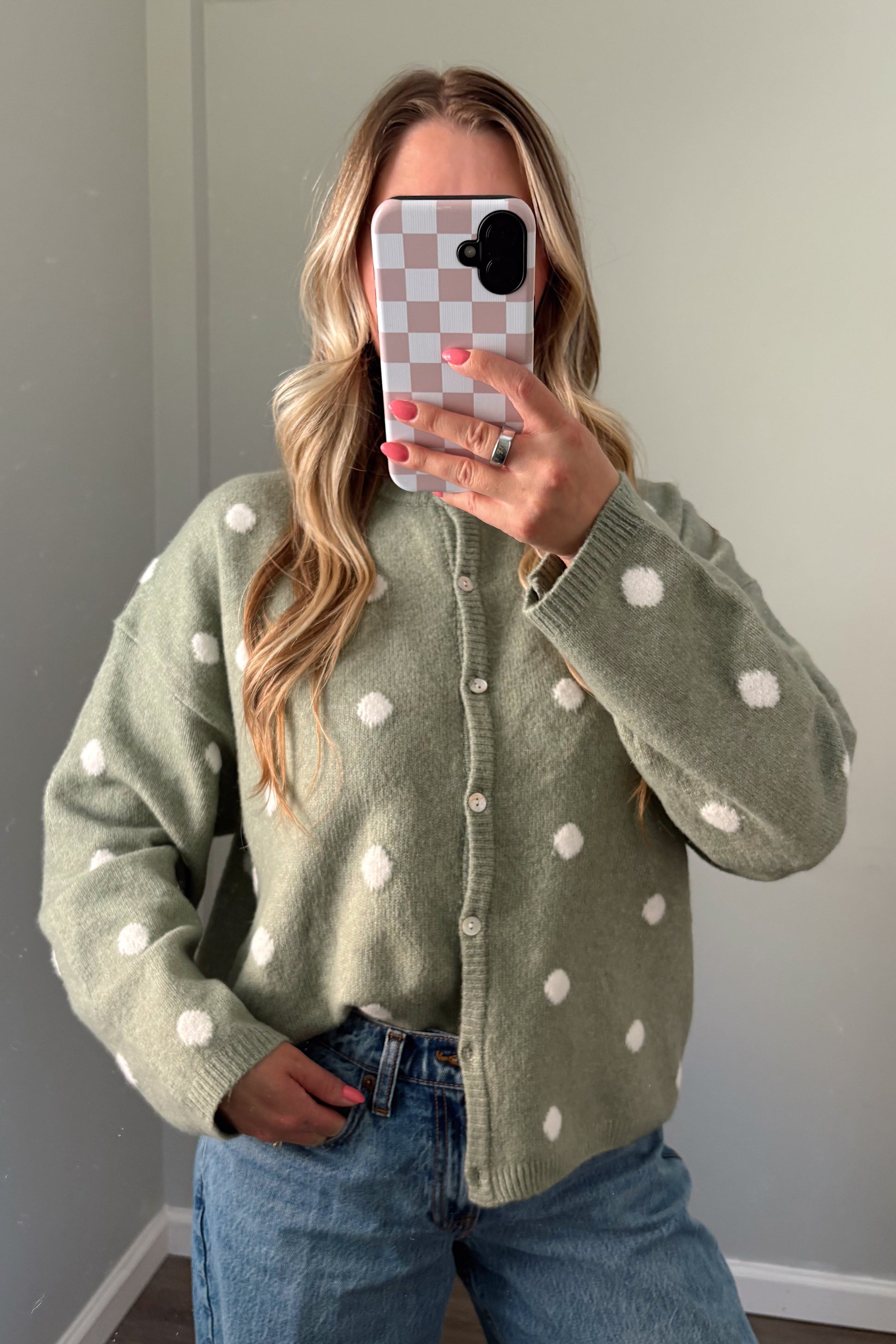 person wearing a sage green polka dot cardigan in a mirror photo