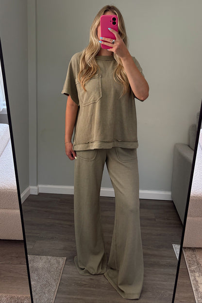 A woman takes a mirror selfie in a room wearing a matching two-piece lounge set consisting of a short-sleeve textured top and wide-leg pants in a muted sage green color.