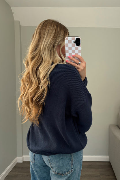 Person wearing a navy sweater and blue jeans taking a mirror selfie.