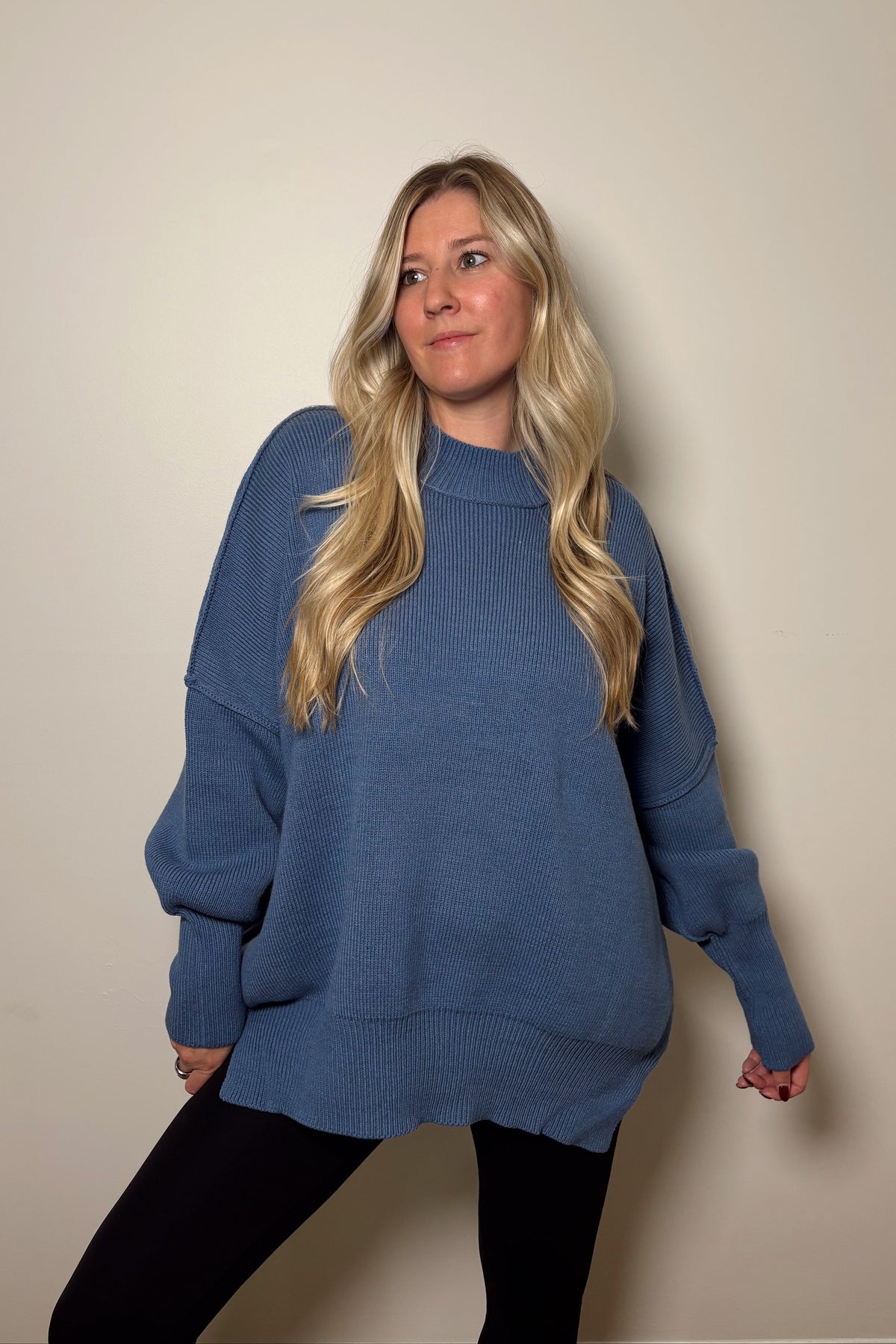 Essential dusty blue oversized sweater styled with black leggings, showing exposed shoulder seams and a relaxed silhouette.

