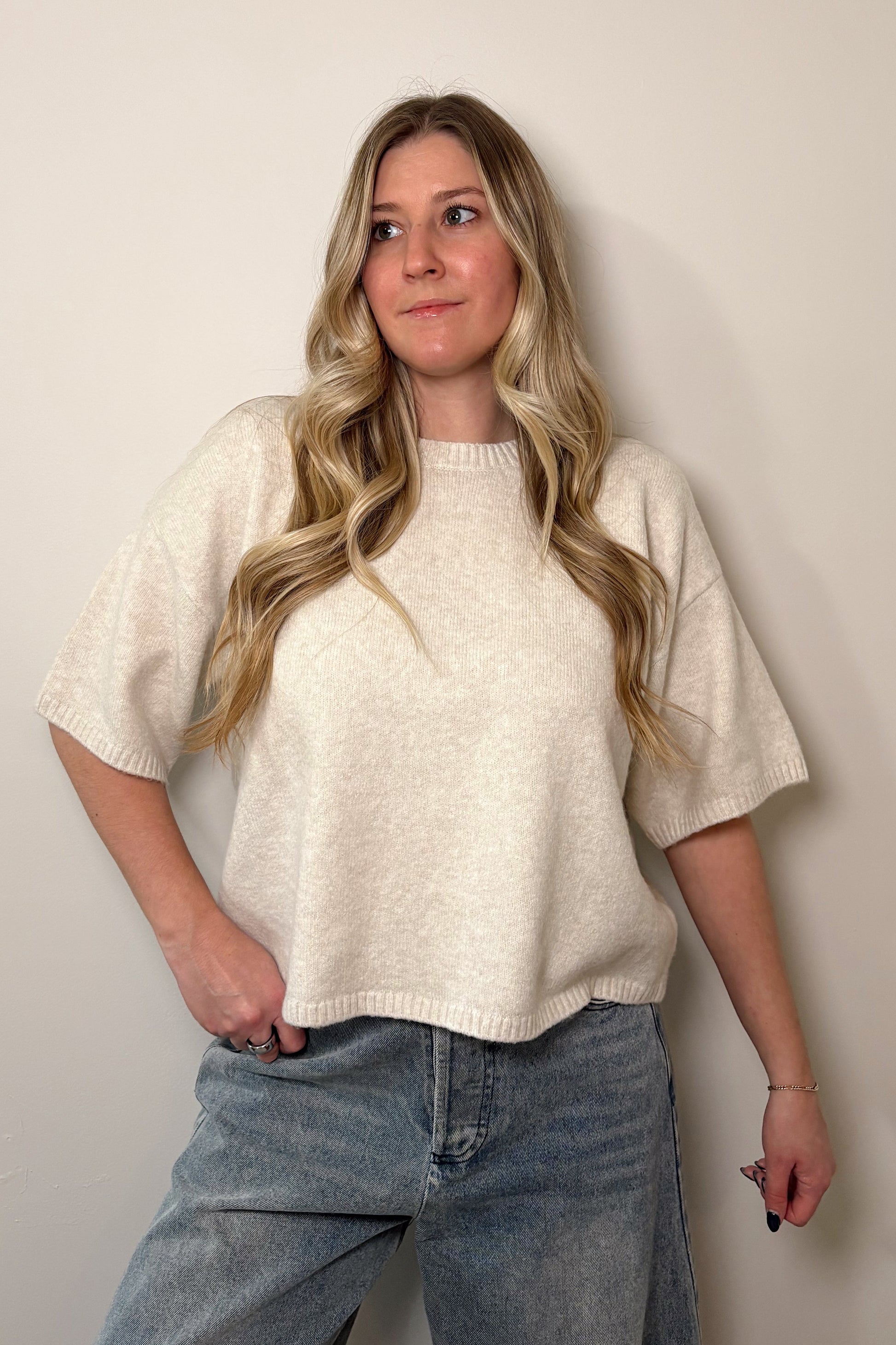 Person wearing a ivory oversized shirt and blue jeans against a plain background