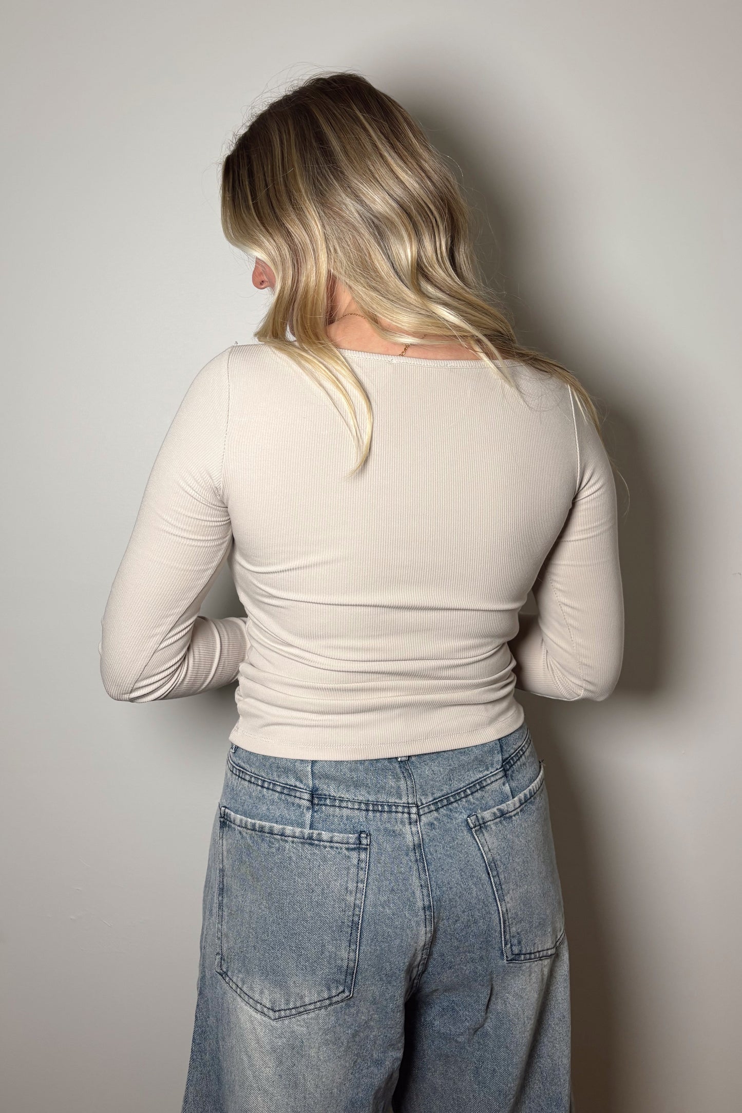 Person wearing a beige long-sleeve top and blue jeans against a plain background