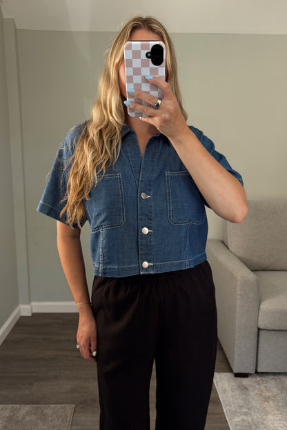 Person wearing a denim shirt taking a mirror selfie in a room with a gray couch.